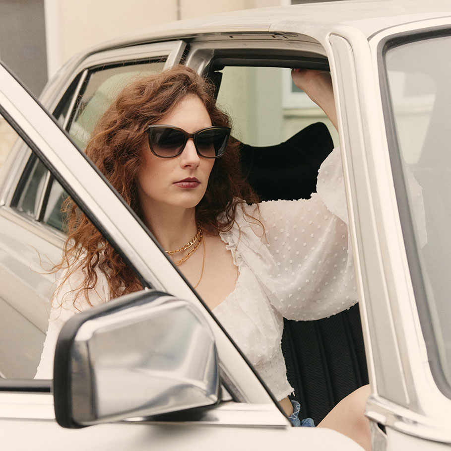 Brünette Frau steigt aus dem Auto und trägt die Sonnenbrille FRAIMS Selena auf dem Weg zum Optiker